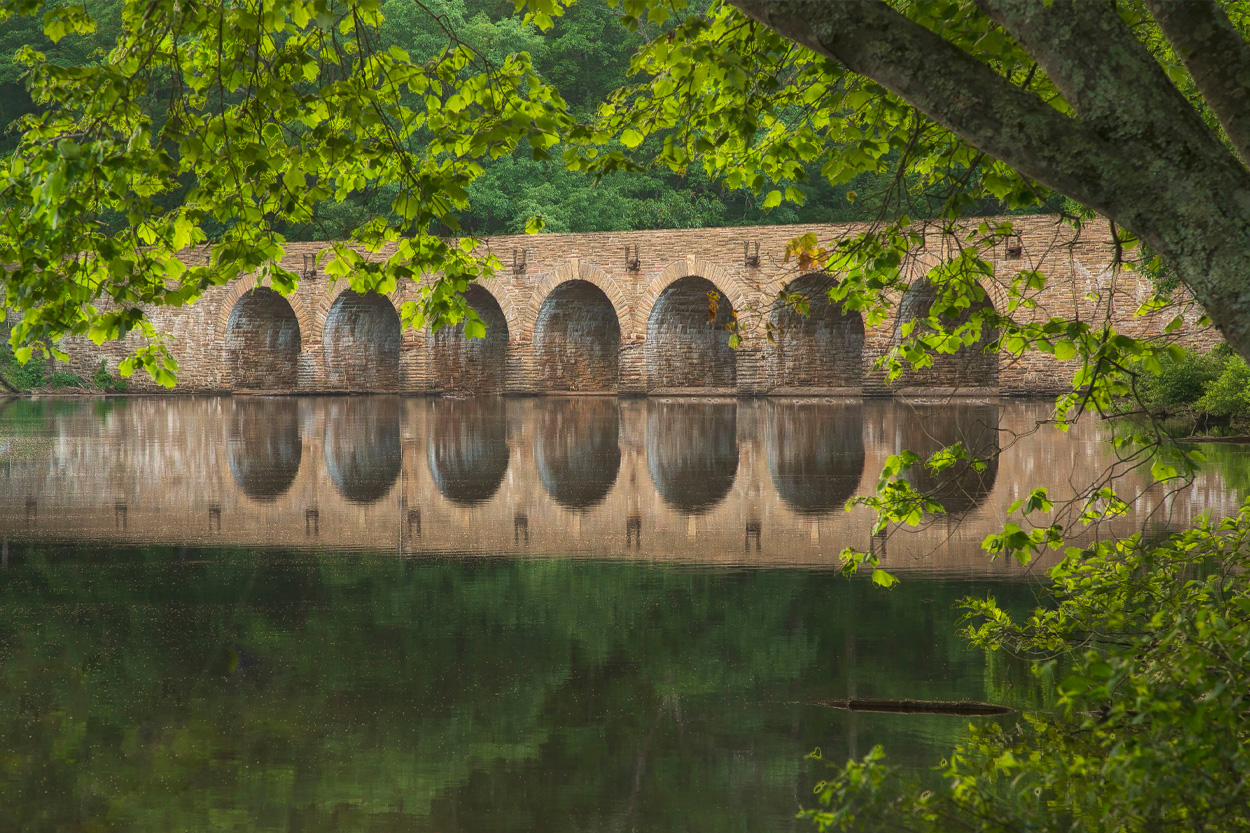 Stone arched bridge reflected in calm water beneath green trees in Crossville, Tennessee