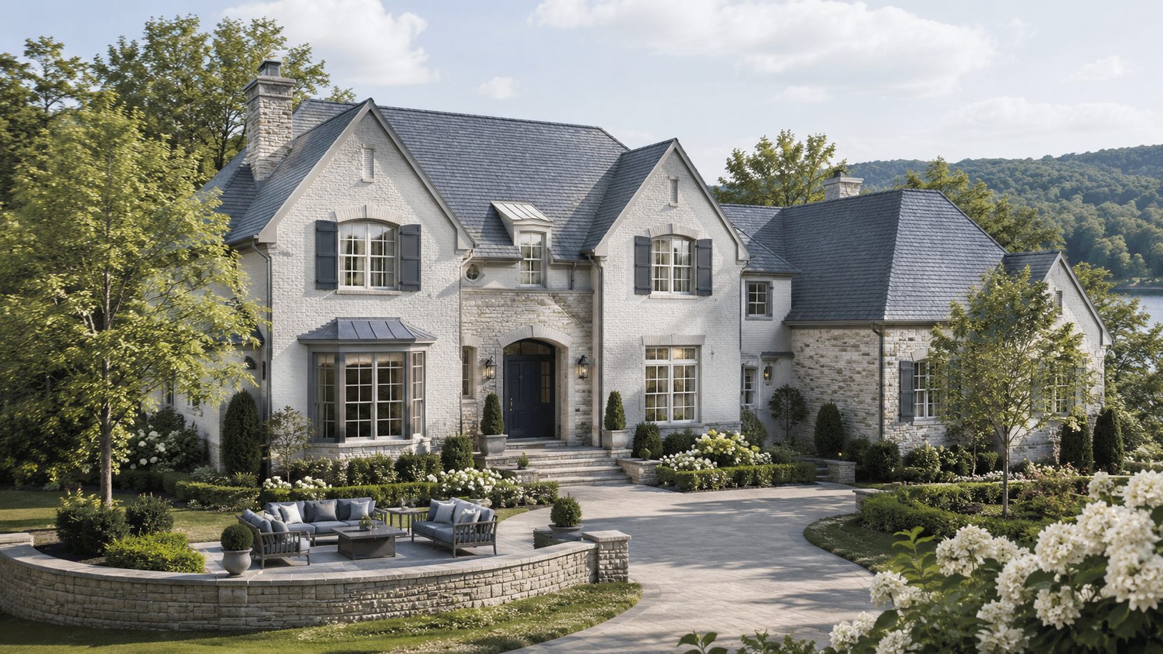 Elegant Knoxville luxury home with light stone exterior, blue-gray shutters, mature landscaping, and wooded East Tennessee surroundings.